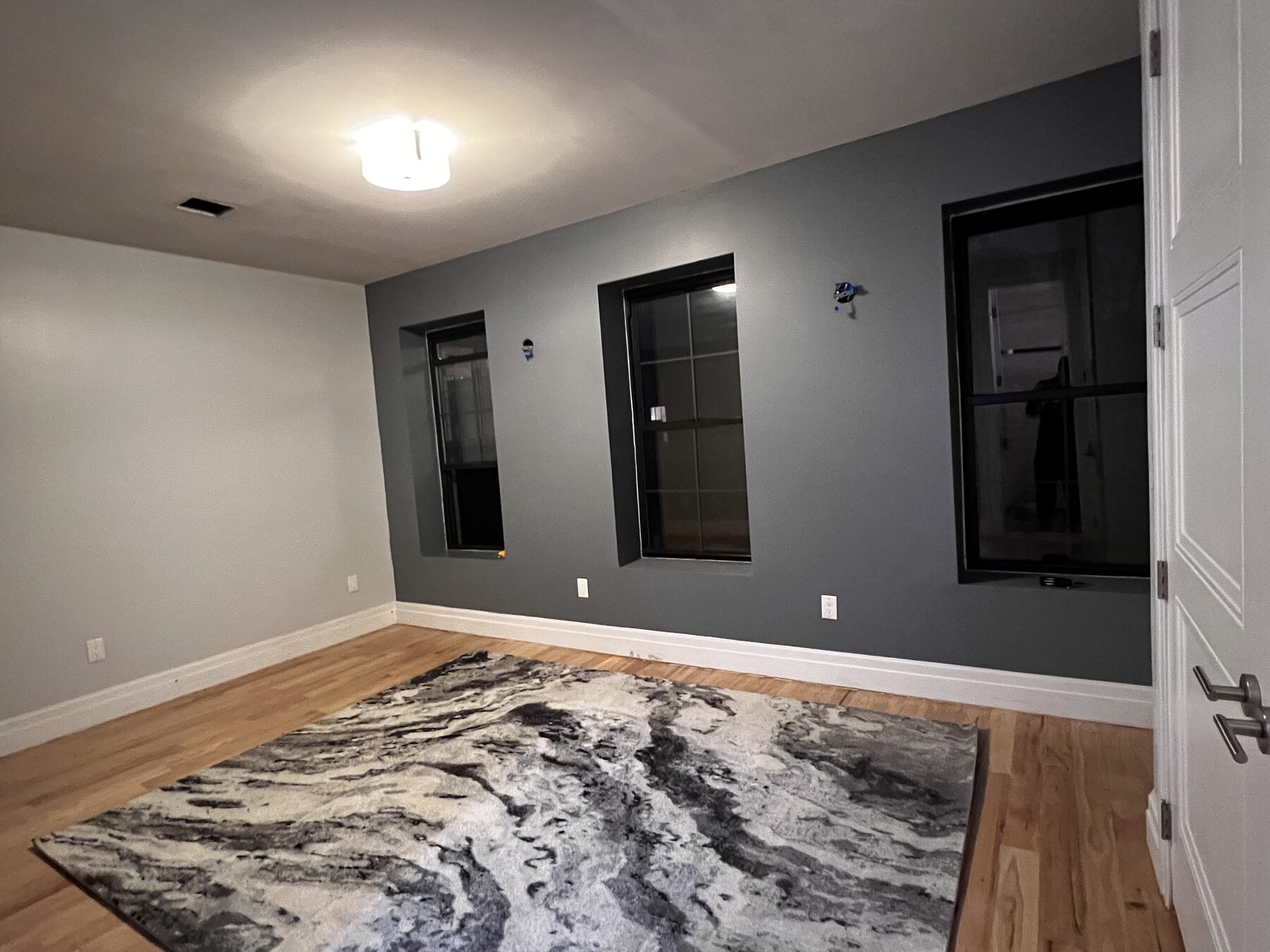 The finished bedroom — charcoal accent wall, refinished floor, marble-patterned rug