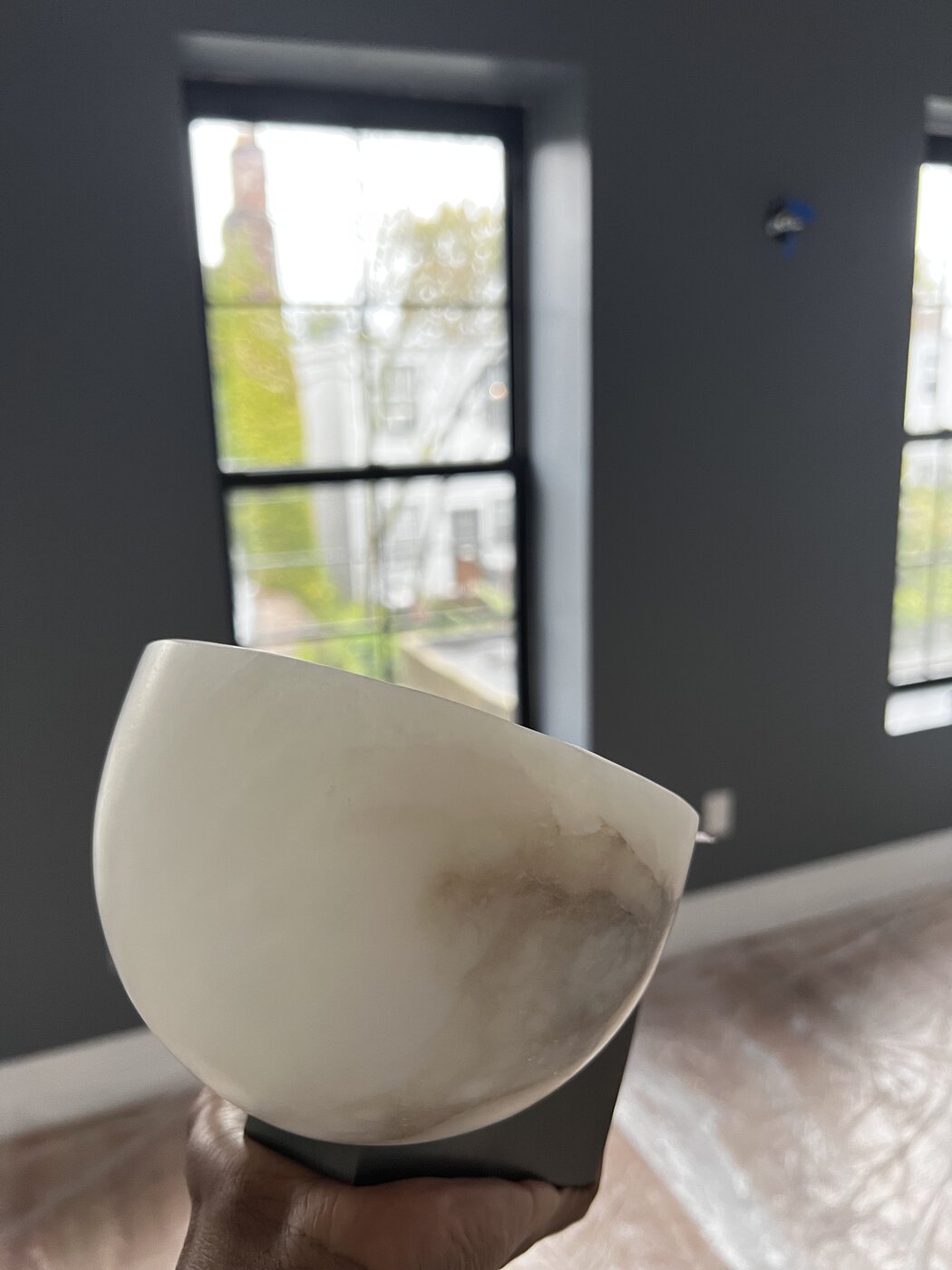The alabaster sconce held up to the freshly painted charcoal wall, the junction box visible behind it, waiting