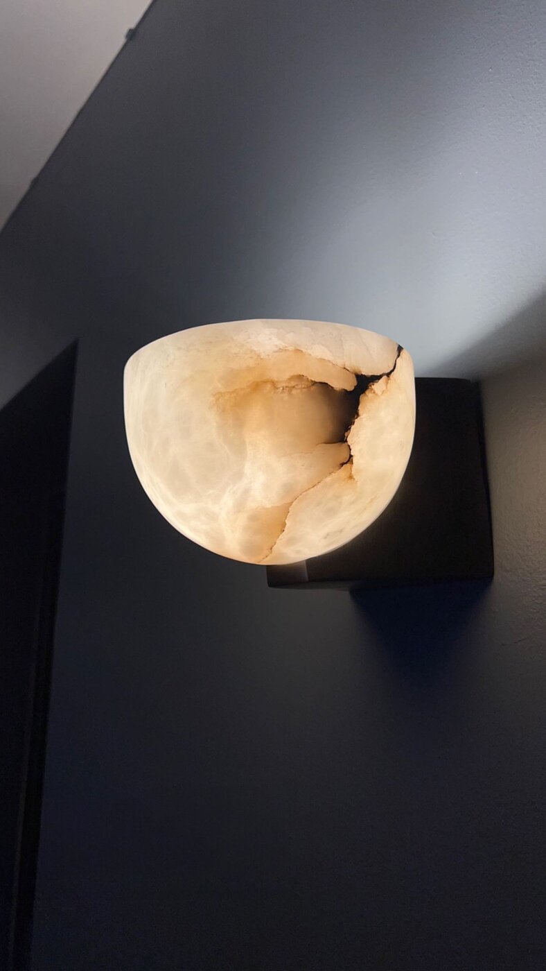 The bedroom at dusk — a lit alabaster sconce against a deep slate accent wall