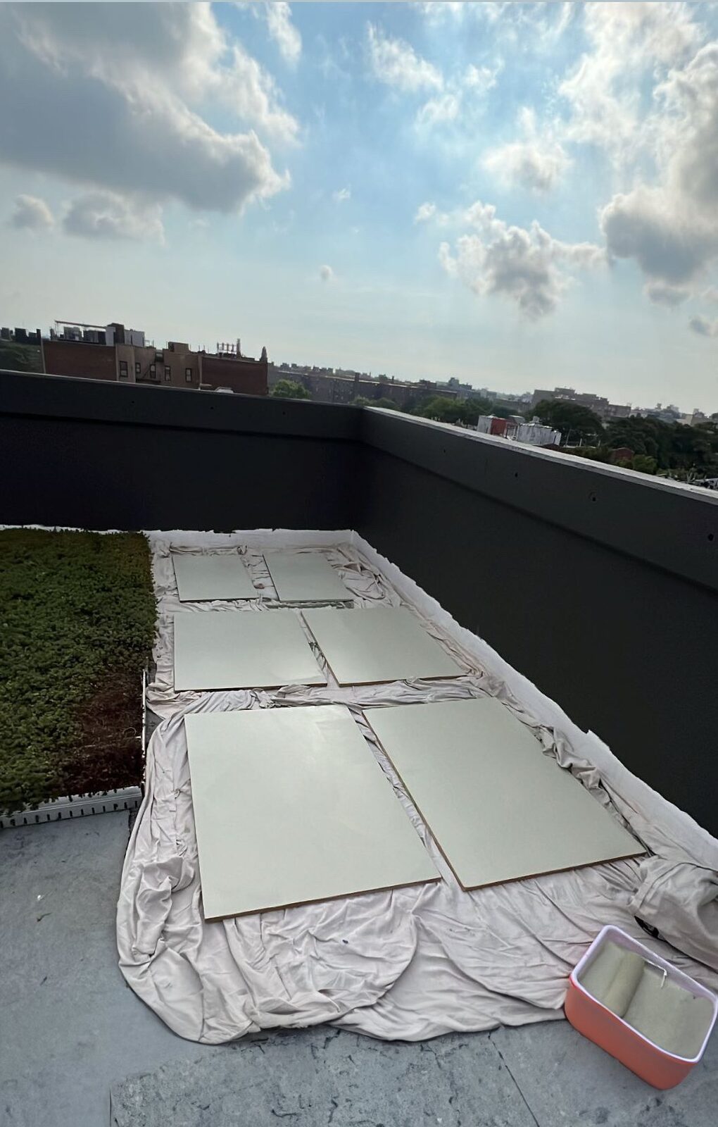 Six MDF panels laid out to dry on a Brooklyn rooftop after their final coat of Sherwin-Williams Grasslands, with the green rooftop garden and city skyline behind